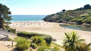A beach with a rocky cliff, a clear sky, and a calm sea.
