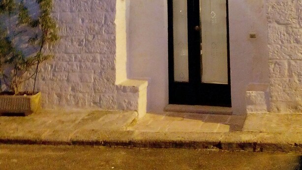 A building with a dark conical roof, a chimney, and a white facade with a black door.