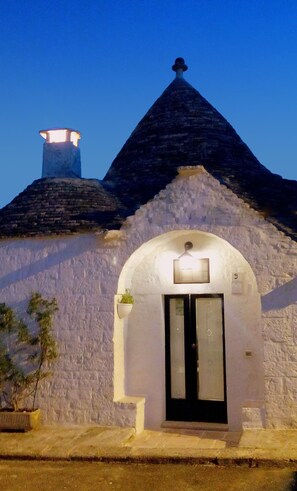 A building with a dark conical roof, a chimney, and a white facade with a black door. - Trullo dell'Aia, a distinctive and unique trullo in the center of Alberobello (Alberobello)