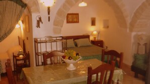 A cozy room with a bed, a dining table with chairs, and a fruit bowl.