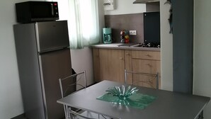 A compact kitchen with a refrigerator, microwave, and coffee maker. There is a dining table with chairs and a decorative glass centerpiece.