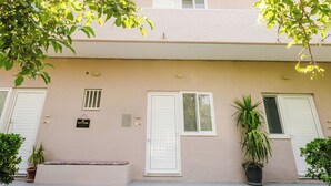 Un bâtiment à deux étages, doté d’une façade sobre, d’une petite fenêtre et d’une porte. Des plantes en pot sont disposées au niveau du rez-de-chaussée.