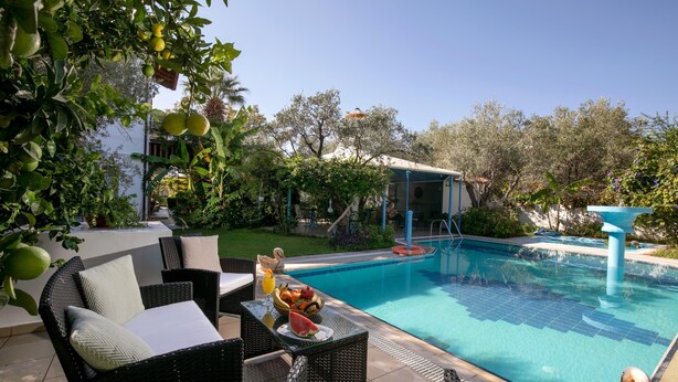 Un espace aménagé au bord de la piscine, avec des meubles en osier, un panier de fruits et une vue sur un bâtiment surmonté d’un dôme.