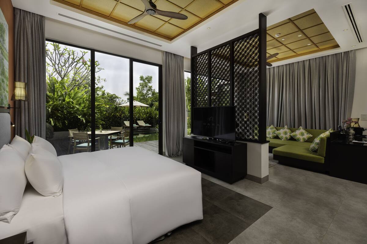 Een moderne hotelkamer met een groot bed, een televisie, een balkon met buitenmeubels en uitzicht op groen.