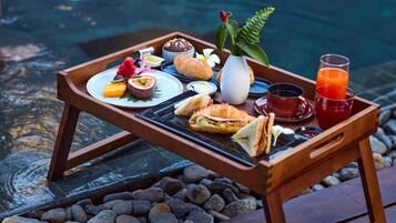 A wooden tray with food and drinks by a pool.