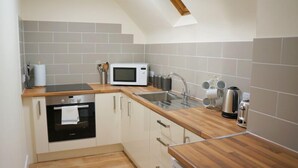 A modern kitchen with grey tiles, a microwave, a sink, and wooden countertops. - Light, Bright Apartment Tucked Away by Bordeaux Harbour (Vale)
