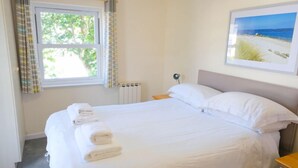 A neatly made bed with white linens and towels, a window with curtains, and a framed picture on the wall. - Light, Bright Apartment Tucked Away by Bordeaux Harbour (Vale)