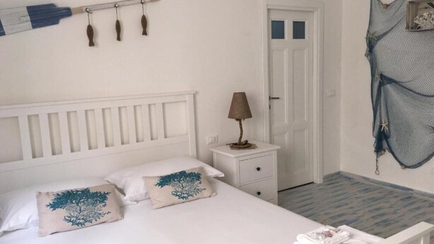 Une chambre à coucher bien rangée, avec un lit, des oreillers, une table de chevet, une lampe, une porte et un moustiquaire accroché au mur.
