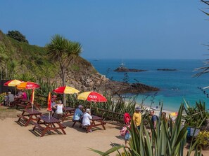 A beach with wooden lounge chairs and red umbrellas, a rocky coastline, and the ocean in the background. - Ground-Floor Apartment in Quiet Coastal Location (Two-Bedrooms) (Vale)