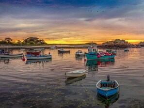 A harbor with several boats anchored, calm water, and a sunset in the background.