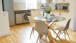A modern kitchen with a dishwasher, washing machine, microwave, and a glass dining table with chairs.