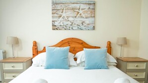 A neatly made bed with two pillows, a wooden headboard, and a wall-mounted artwork of starfish and seashells.