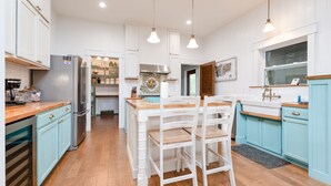 A modern kitchen with white cabinetry, wooden countertops, and a dining area with white chairs. - Brand New 3 Bedroom, Pet Friendly Amazing Bay View Home (St George Island)