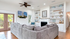 A living room with a grey sectional sofa, a fireplace, and a bookshelf with decorative items. - Brand New 3 Bedroom, Pet Friendly Amazing Bay View Home (St George Island)
