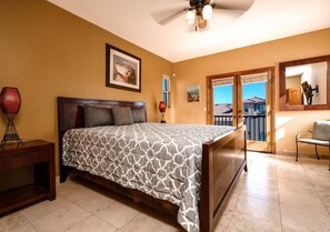 Ein Schlafzimmer mit Bett, Nachttisch, Sessel, Deckenventilator und einem Balkon mit Blick.