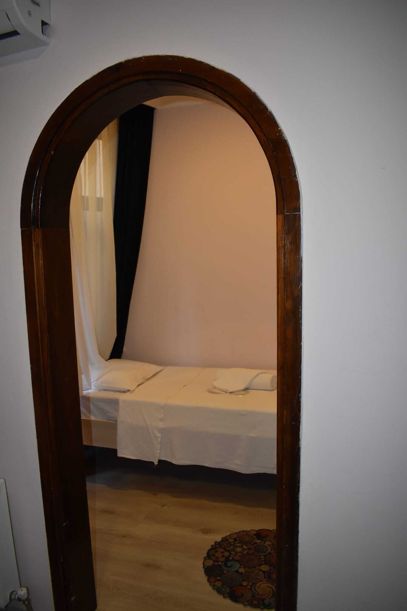 A narrow doorway leading to a room with a bed, a wooden floor, and a patterned rug.