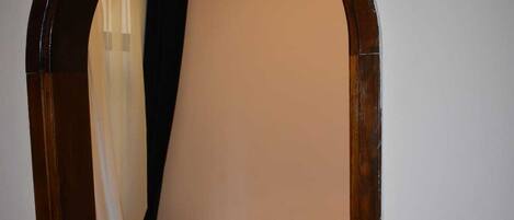 A narrow doorway leading to a room with a bed, a wooden floor, and a patterned rug.