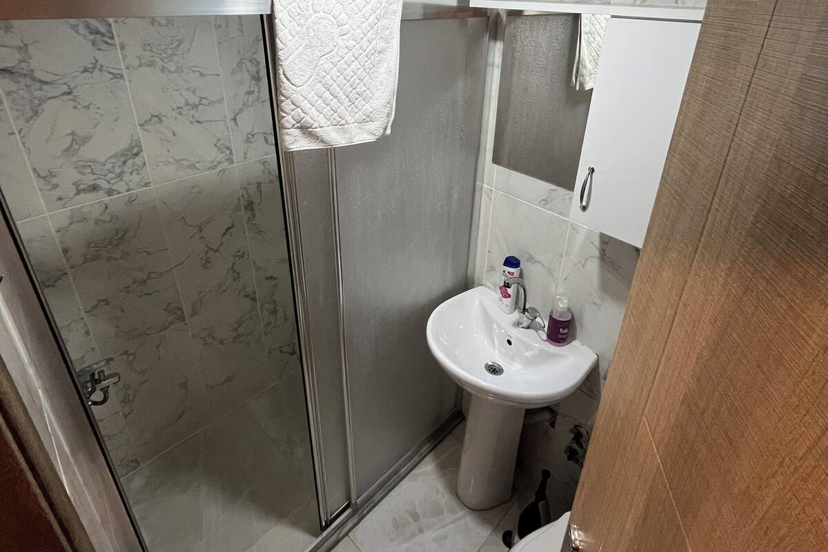 A bathroom with a glass-enclosed shower, a sink with a mirror above it, and a toilet.