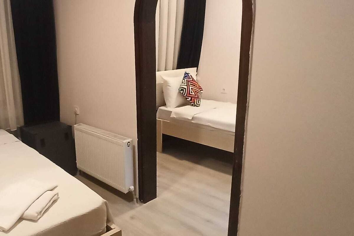 A hotel room with a bed, a bedside table, a radiator, and a mirror.