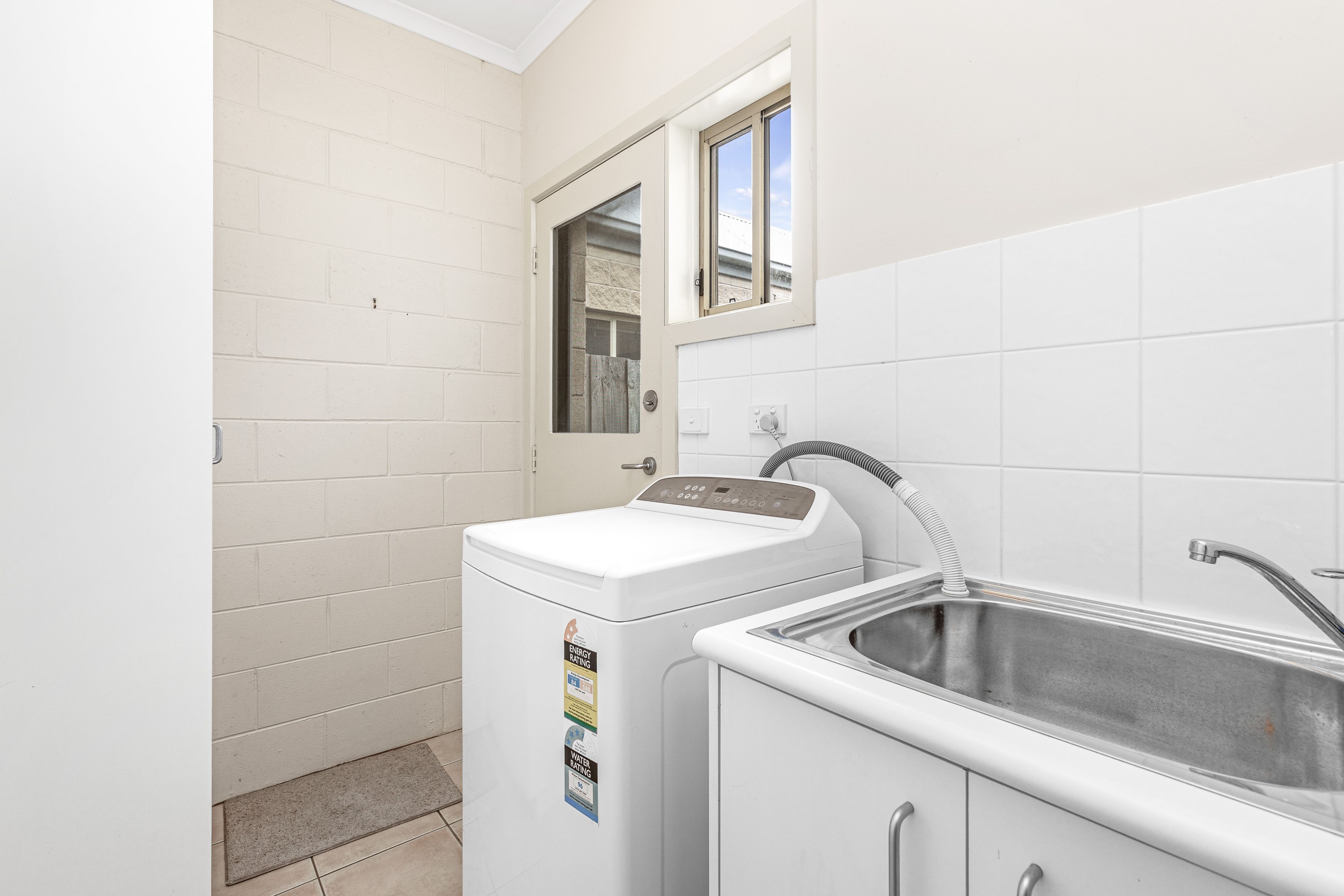 A compact laundry room with a washing machine, a sink, and a window.