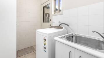A compact laundry room with a washing machine, a sink, and a window.