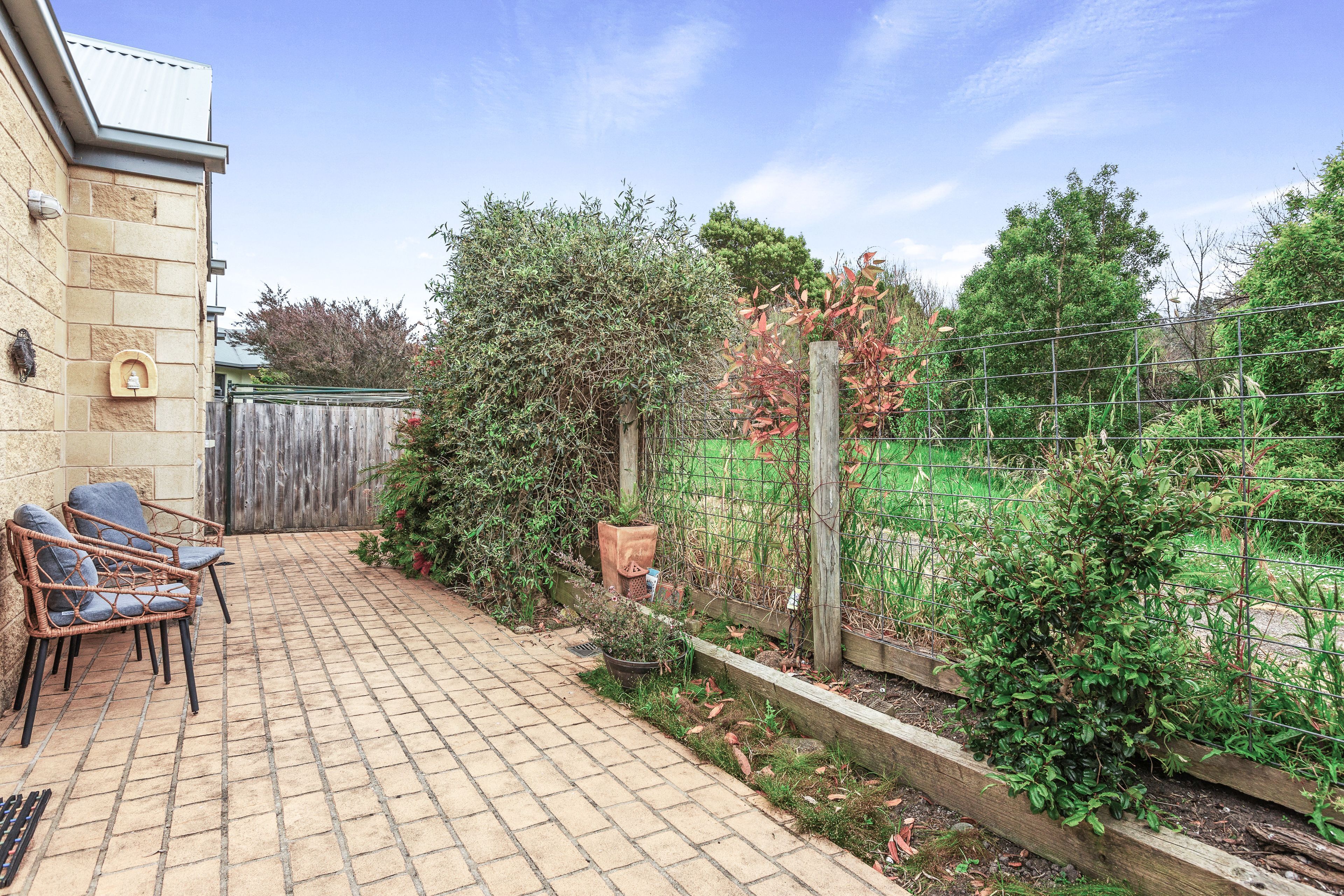 Une terrasse avec un sol en briques, une clôture en bois et un espace jardin agrémenté de diverses plantes et d’un poteau en bois.