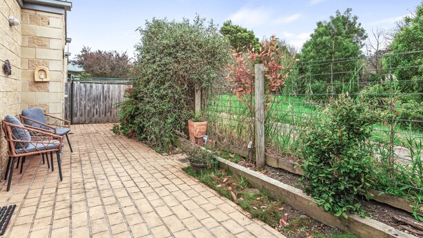 A patio with a brick floor, a wooden fence, and a garden area with various plants and a wooden post.