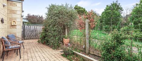 A patio with a brick floor, a wooden fence, and a garden area with various plants and a wooden post.