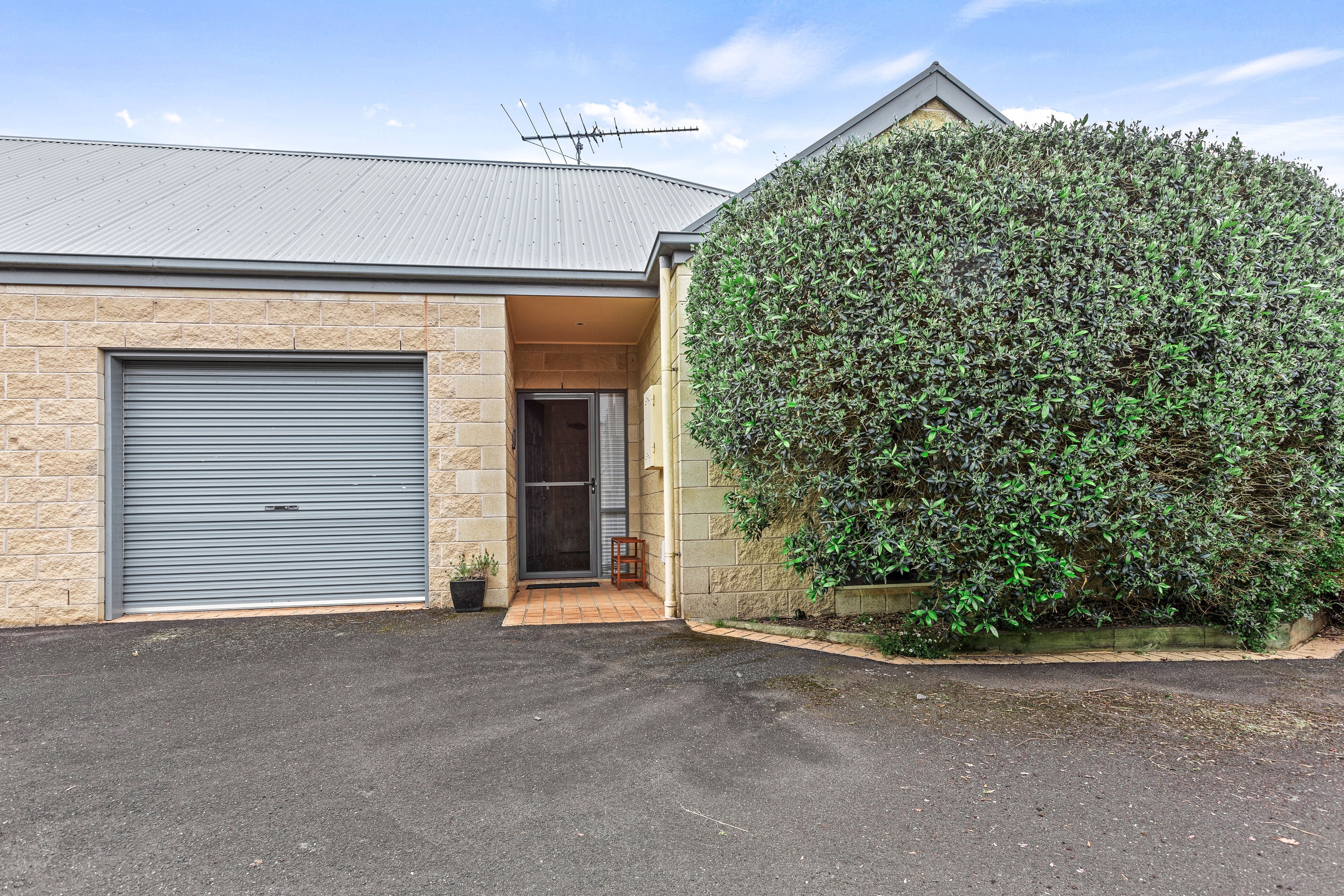 A residential building with a garage door, a small entrance with a door, and a large hedge.