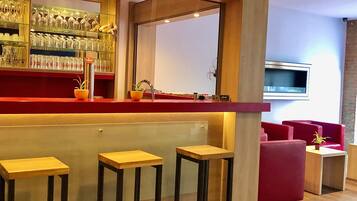 Eine Bar mit Hockern, einer Theke mit Gläsern und einem an der Wand montierten Fernseher.