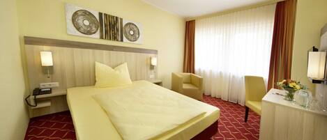 A hotel room with a large bed, a desk with a chair, a TV, and artwork on the wall.