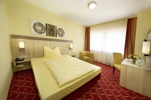 A hotel room with a large bed, a desk with a chair, a TV, and artwork on the wall. - Montivo Hotel Köln-Bonn Airport (Troisdorf)