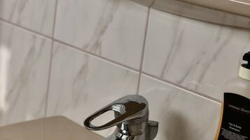 A bathroom with a marble wall, a yellow plant in a bowl, a chrome faucet, and a bottle of shampoo.