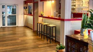 A modern kitchen with a red countertop, three stools, and a bar area with glassware. - Montivo Hotel Köln-Bonn Airport (Troisdorf)