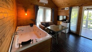 L’intérieur d’un chalet en bois comprend une grande baignoire, un canapé, un téléviseur et une table à manger.