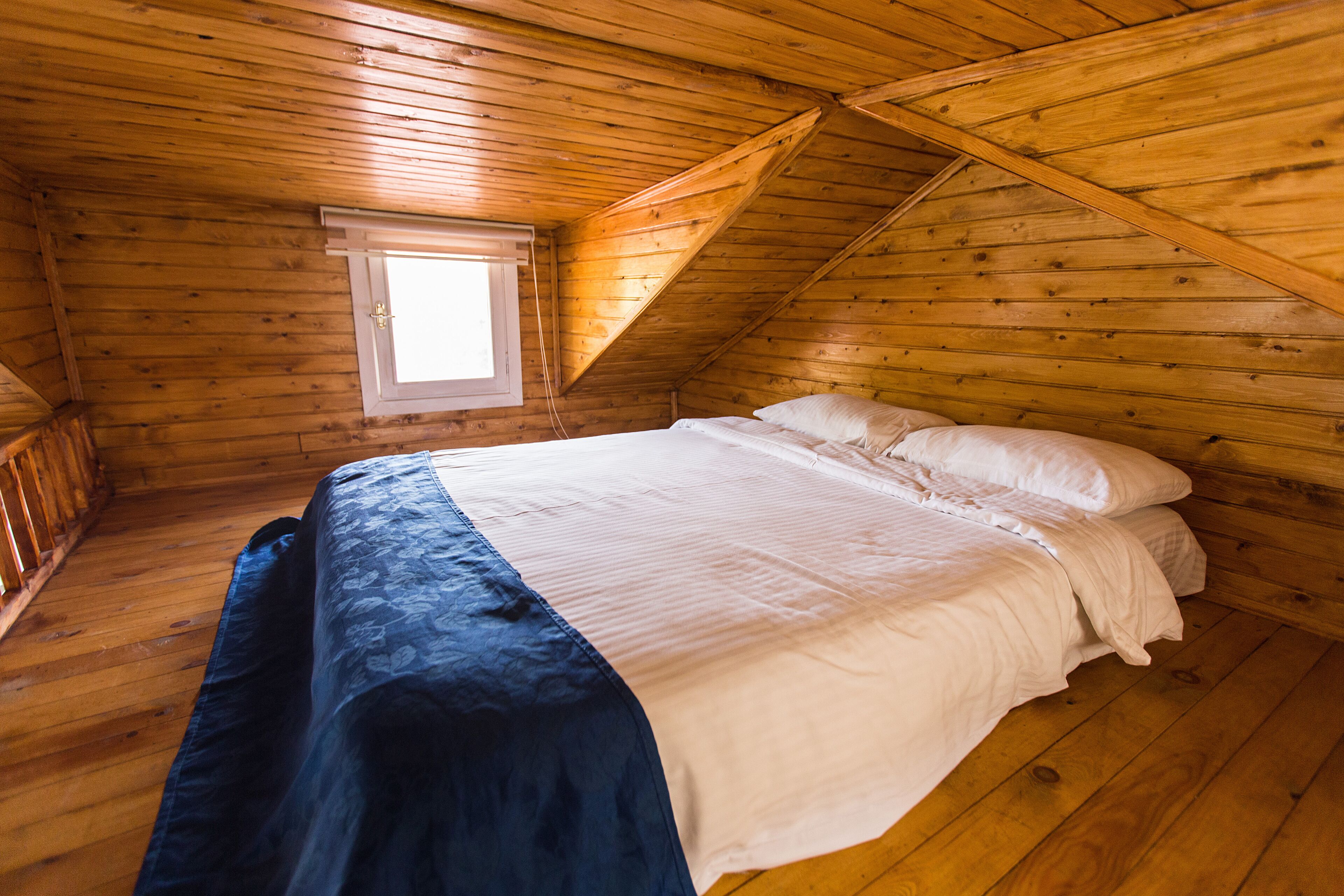 A wooden cabin bedroom with a bed, a window, and a sloped ceiling.