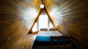 Une pièce triangulaire en bois, avec un lit, des oreillers et un luminaire suspendu.