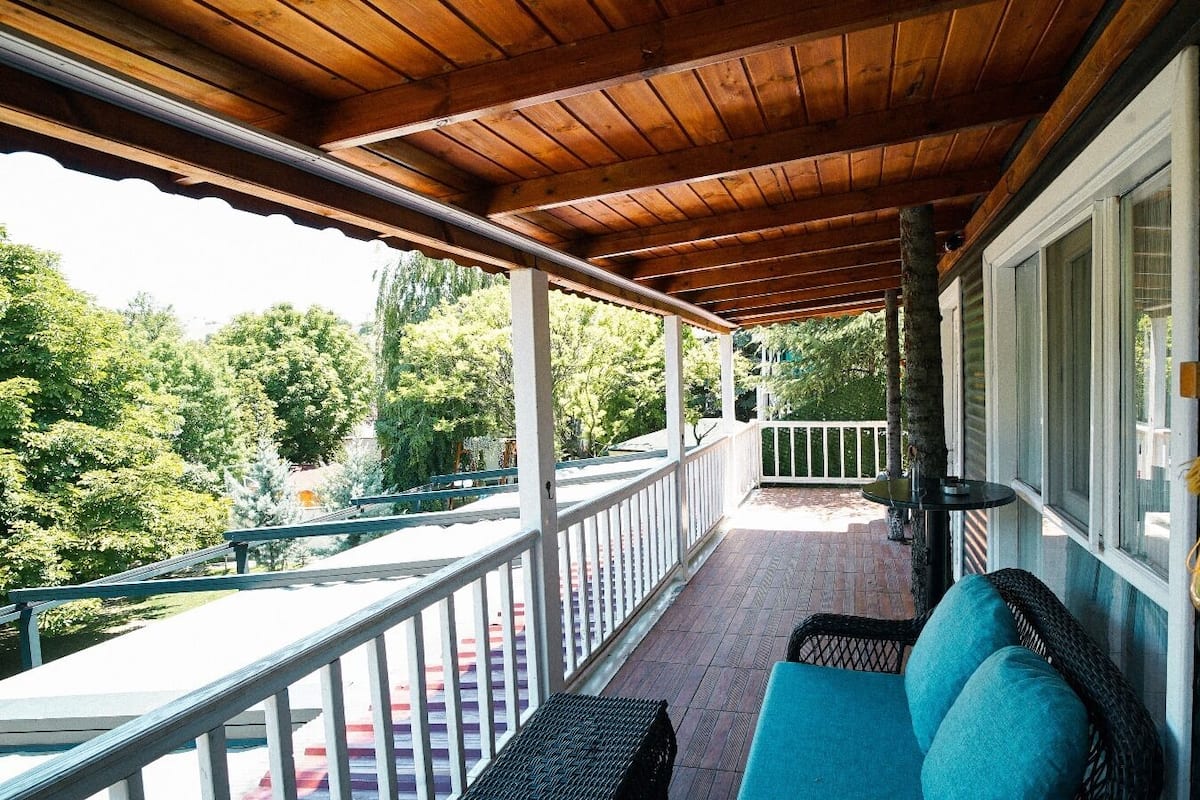 A covered porch with a seating area, a railing, and a view of greenery.