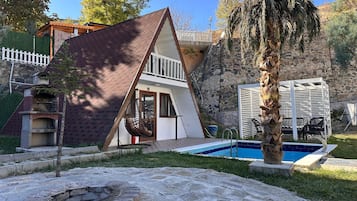 Experience a serene retreat surrounded by lush greenery and a stone wall, with a unique triangular roof and outdoor pool.
