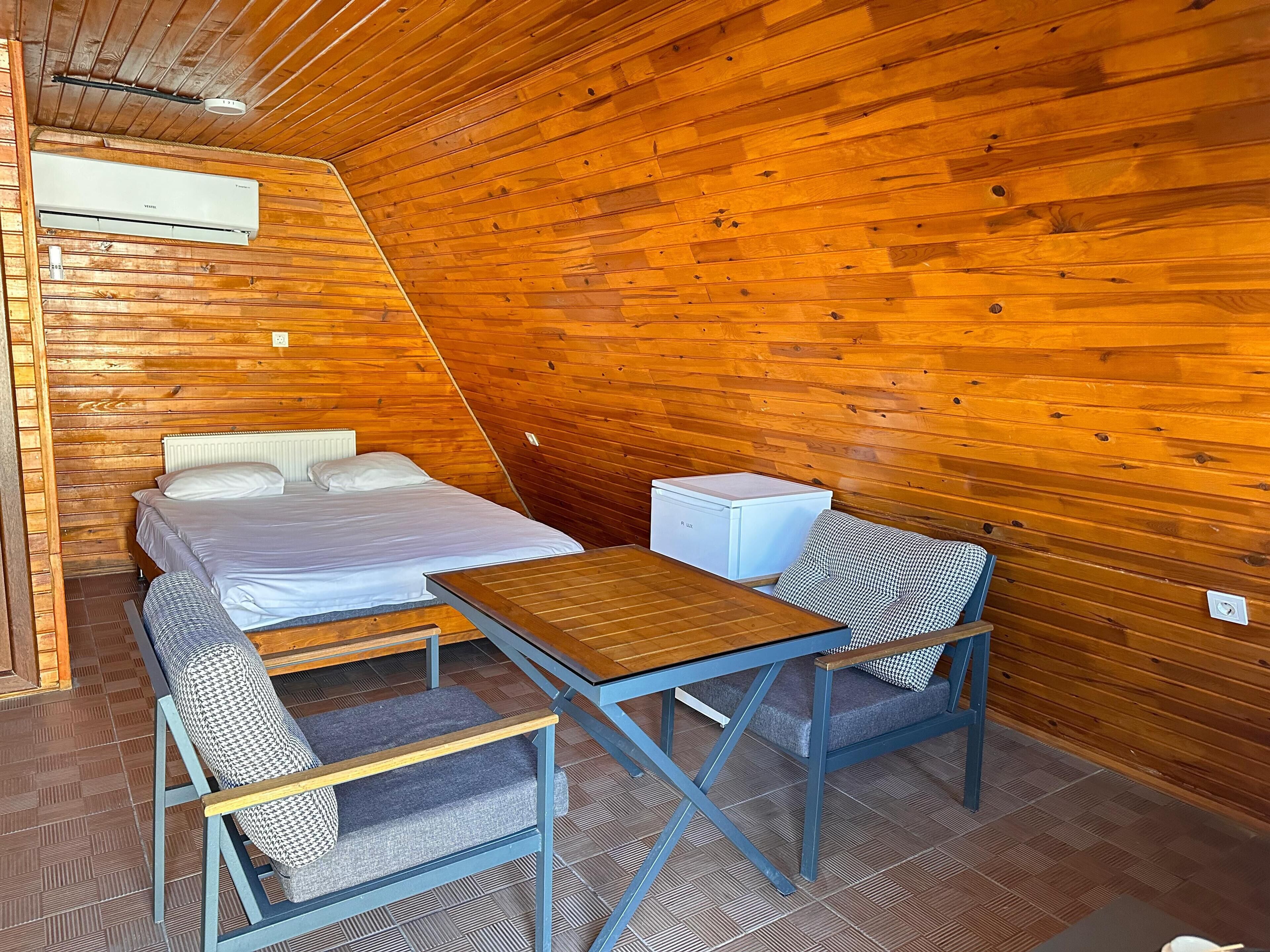 Um quarto acolhedor, com painéis de madeira, uma cama, uma mesinha e uma cadeira.
