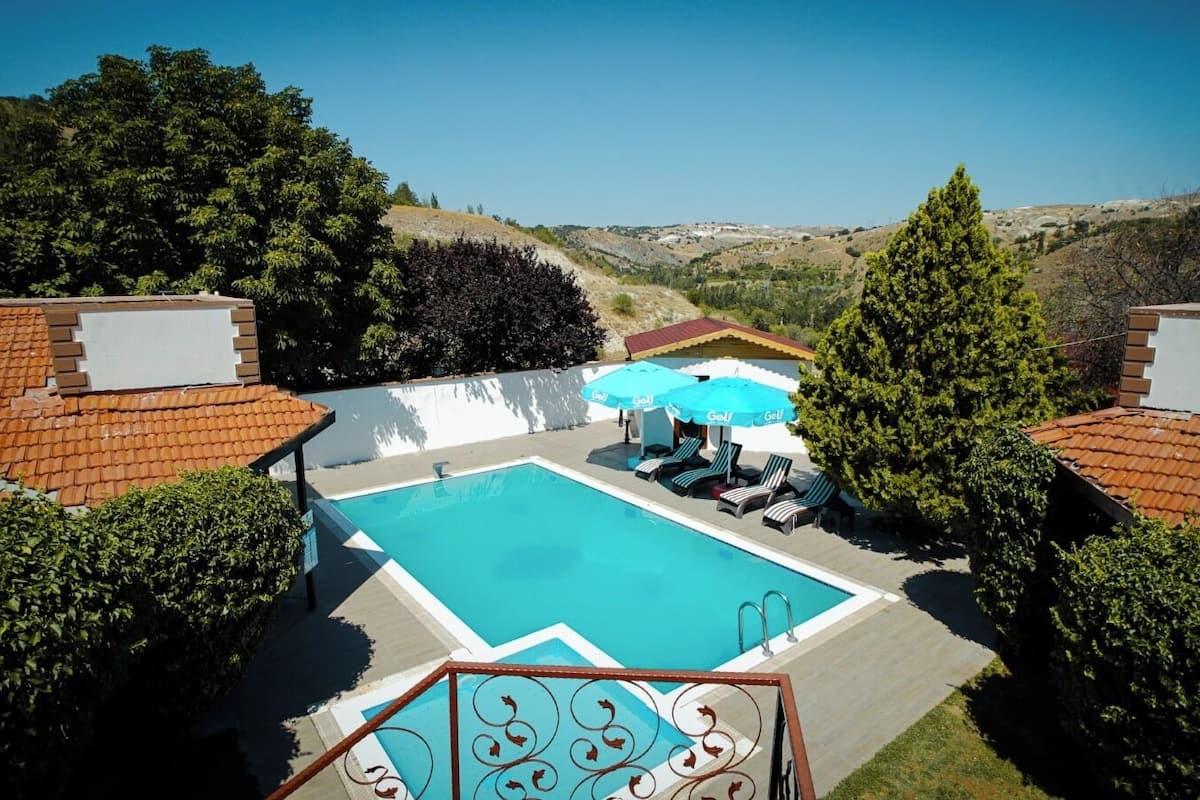 A swimming pool with lounge chairs and umbrellas, surrounded by greenery and hills.