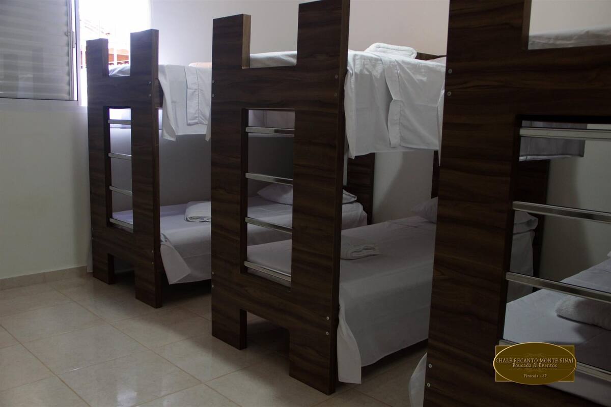 A room with bunk beds, each with a white sheet and a hanging towel.