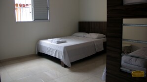 A single bed with a wooden headboard, a small bedside table, and a window with closed blinds. - Chale Recanto Monte Sinai (Piracaia)