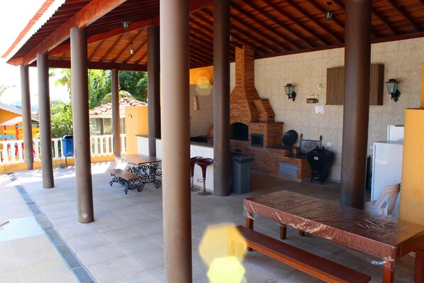 Un área de patio techada al aire libre con chimenea de ladrillo, bancos de madera y piso de baldosas.