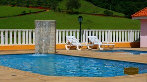A swimming pool with a waterfall feature, surrounded by a white fence and a lamp post.
