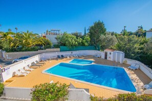 A swimming pool with lounge chairs and a lifeguard tower, surrounded by greenery and a clear sky.