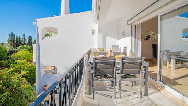 Ein Balkon mit Tisch und Stühlen, mit Blick auf einen Garten und ein Gebäude mit Schornstein.