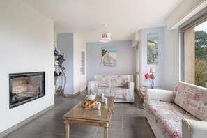 A living room with a fireplace, a sofa, a coffee table with pastries, and artwork on the walls.