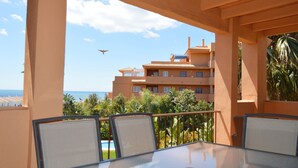Un balcón con una mesa y sillas de vidrio, con vistas a una piscina y un edificio con varios balcones.