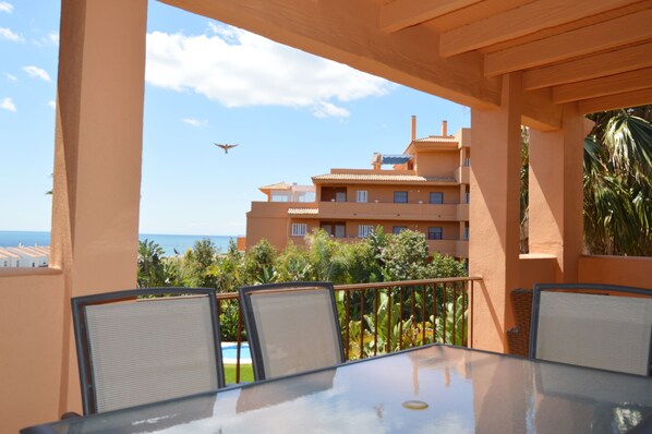 Ein Balkon mit Glastisch und Stühlen, der einen Pool und ein Gebäude mit mehreren Balkonen überblickt.